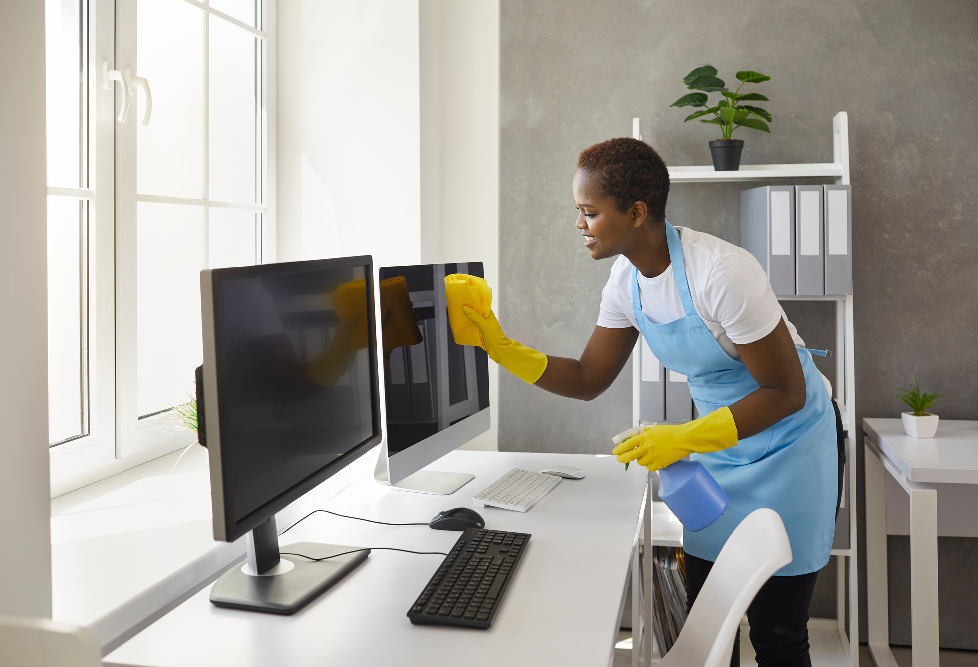Happy Woman from Janitorial Cleaning Service Wiping Computer Screens in Modern Office
